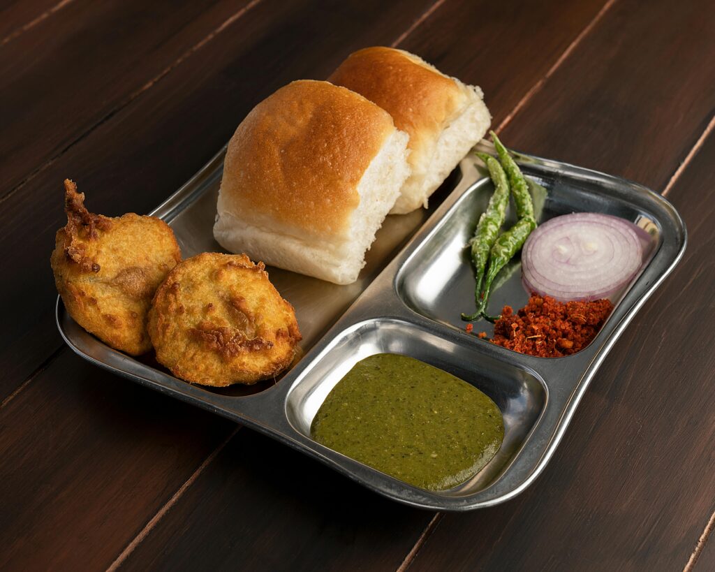 मुंबई में कम बजट यात्रा: कम खर्च में घूमने के टिप्स और गाइड 1 Delicious Maharashtrian Vada Pav served with chutney and spices on a stainless steel plate.