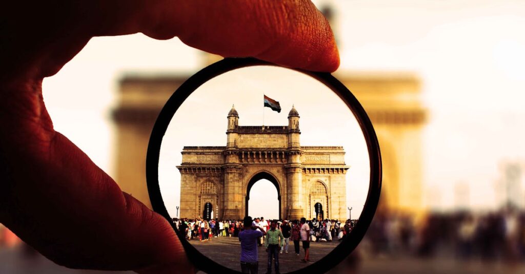 मुंबई में कम बजट यात्रा: कम खर्च में घूमने के टिप्स और गाइड 2 Artistic view of the Gateway of India through a camera lens filter with vibrant colors and bustling crowd.