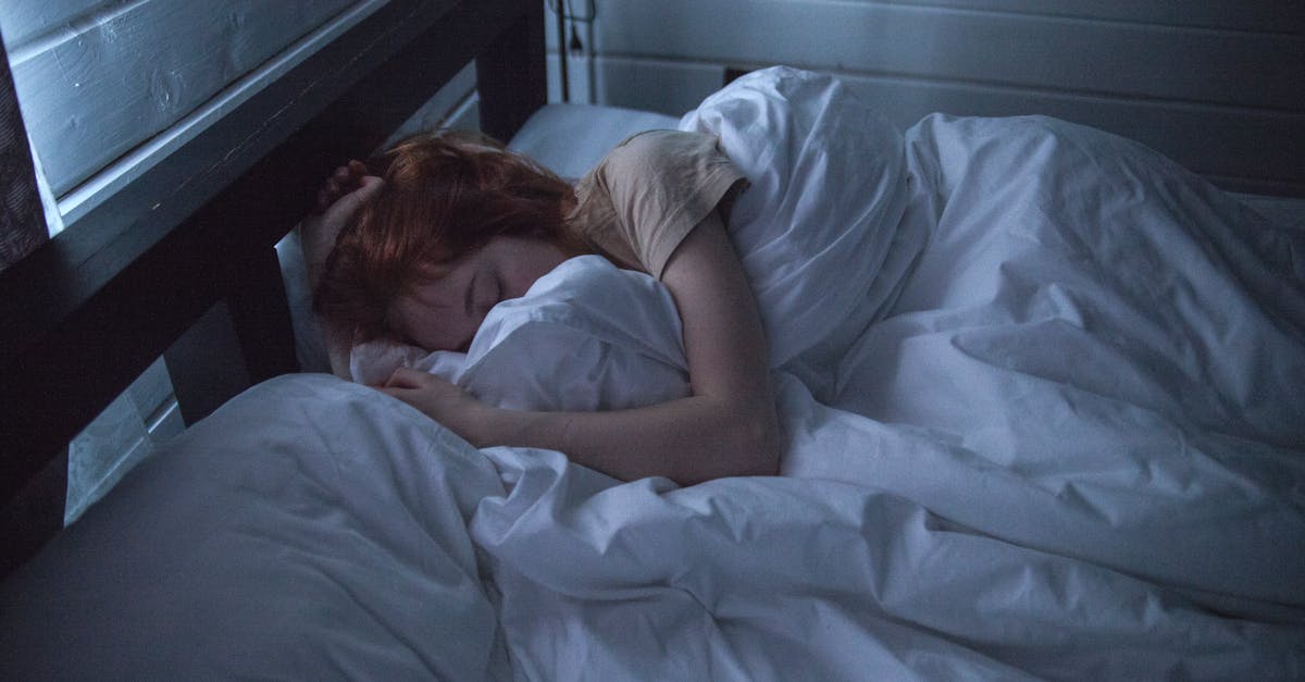 A woman sleeping peacefully in a cozy bedroom, enveloped by soft white sheets, under the gentle glow of night lighting.