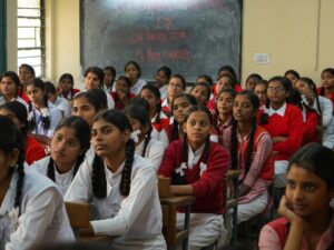 Group of Indian schoolgirls in uniform attentively listening in a classroom setting.