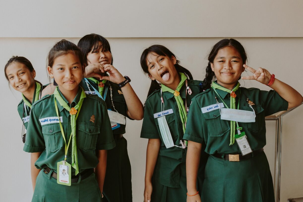 Group of girls in scout uniforms smiling and posing for the camera, showing heart and peace signs.
