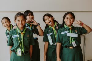 Group of girls in scout uniforms smiling and posing for the camera, showing heart and peace signs.