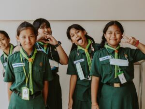 Group of girls in scout uniforms smiling and posing for the camera, showing heart and peace signs.
