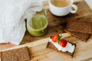 Start your day with a nutritious breakfast featuring rye toast with cream cheese and strawberries, paired with green juice and coffee.