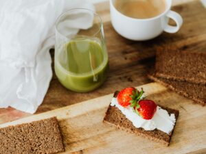Start your day with a nutritious breakfast featuring rye toast with cream cheese and strawberries, paired with green juice and coffee.