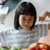 A happy child drinking milk and flexing muscles, promoting a healthy breakfast habit.