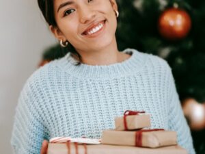 Content young ethnic female with present boxes looking at camera against fir tree during New Year holiday in house क्रिसमस उपहार और 'जीरो-वेस्ट' दर्शन: खुशियाँ बाँटने का एक नया और टिकाऊ तरीका