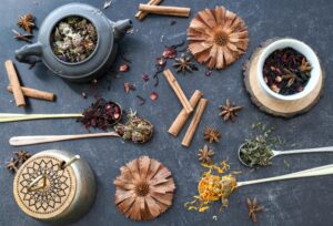 A flat lay of various herbal tea ingredients, spices, and rustic utensils on dark surface.