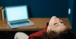 Woman sitting back in chair at a wooden desk with laptop in a cozy, artistic office space. करियर में 'क्वाइट क्विटिंग' क्यों कर रही हैं महिलाएँ? काम और ज़िंदगी के बीच संतुलन की नई परिभाषा