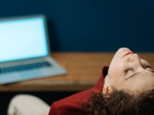 Woman sitting back in chair at a wooden desk with laptop in a cozy, artistic office space. करियर में 'क्वाइट क्विटिंग' क्यों कर रही हैं महिलाएँ? काम और ज़िंदगी के बीच संतुलन की नई परिभाषा