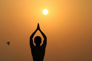 A serene silhouette of a person meditating with hands raised towards the sunset.