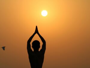 A serene silhouette of a person meditating with hands raised towards the sunset.