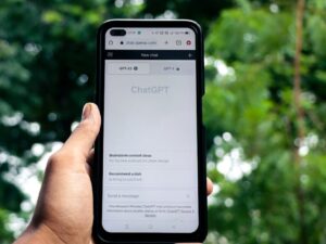 Close-up of a hand holding a smartphone displaying ChatGPT outdoors. एआई बॉट के लिए एडवांस प्रॉम्प्ट इंजीनियरिंग: अपने बॉट को 'जीनियस' कैसे बनाएं?