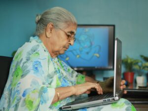 Elderly Indian woman in floral saree using a laptop at home. 2026 में महिलाओं के लिए सर्वश्रेष्ठ वर्क-फ्रॉम-होम बिजनेस आइडियाज: घर से सफलता का सफर