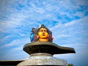 Vibrant three-headed Shiva statue under a blue sky in Pokhara, Nepal.