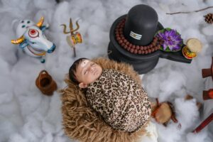 A serene baby wrapped in a leopard-print swaddle lies amidst symbolic Hindu elements.