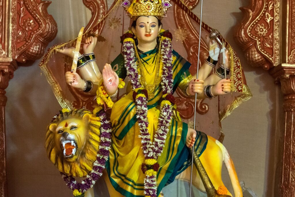 Colorful statue of Goddess Durga holding weapons, adorned with garlands in a Mumbai temple.