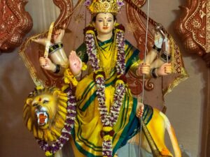 Colorful statue of Goddess Durga holding weapons, adorned with garlands in a Mumbai temple.